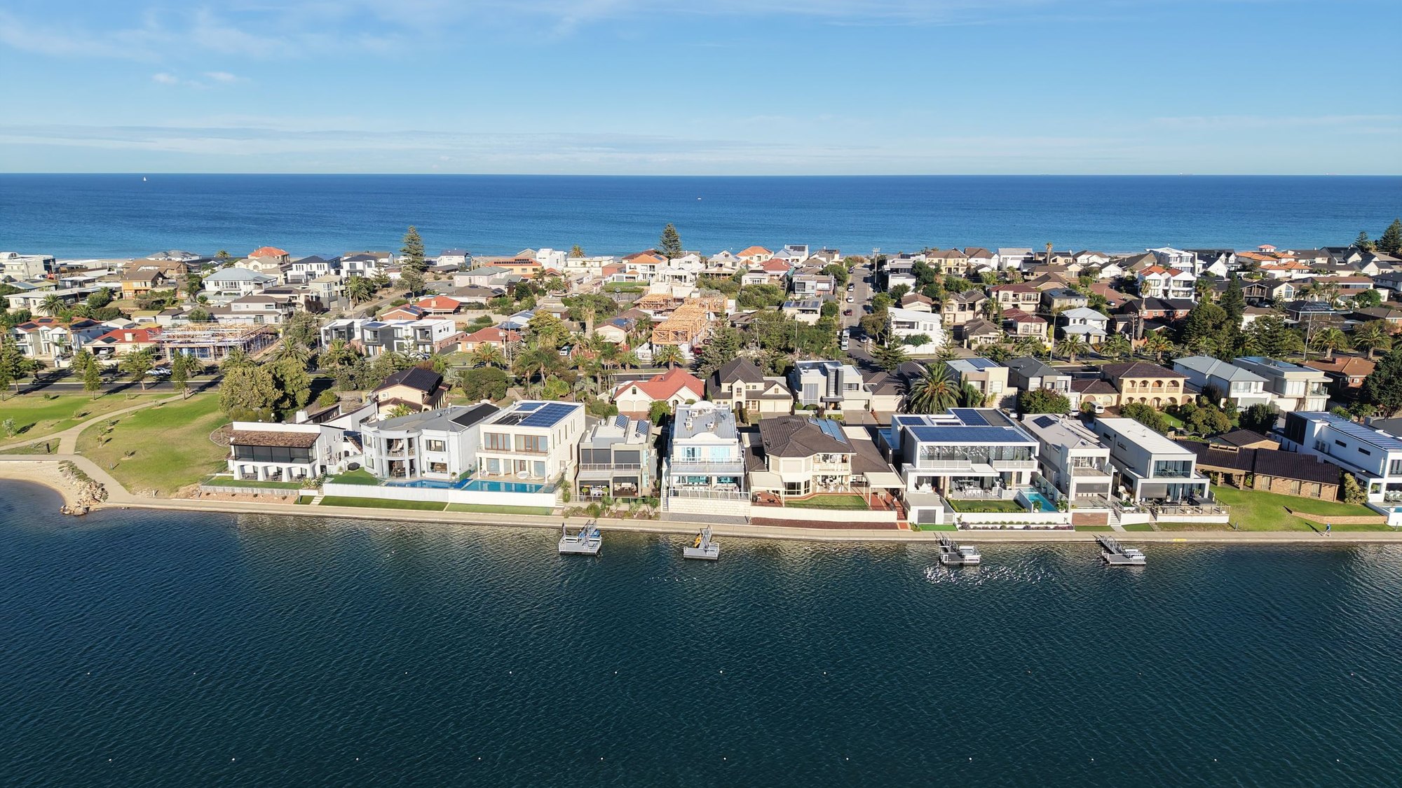 Aerial view of an Australian coastal suburb, waterfront homes along the water with the open ocean beyond.