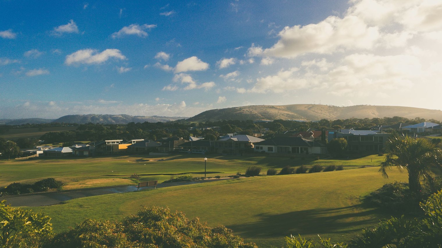 A regional Australian town on the edge of open country, housing backing onto parkland with hills on the horizon.