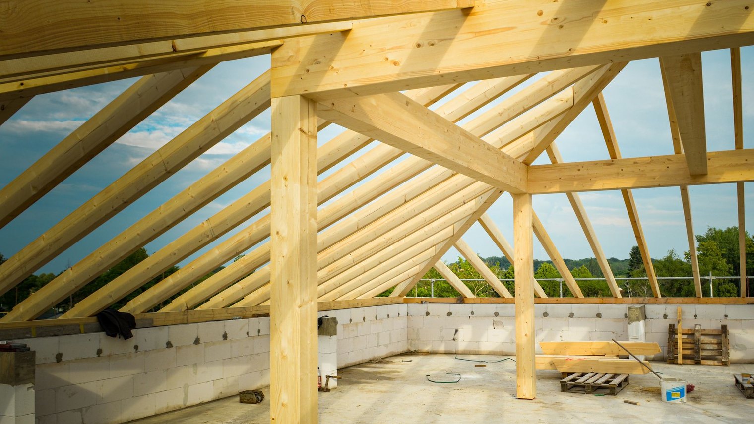 Timber roof trusses and beams on a partially built home, open to the sky.