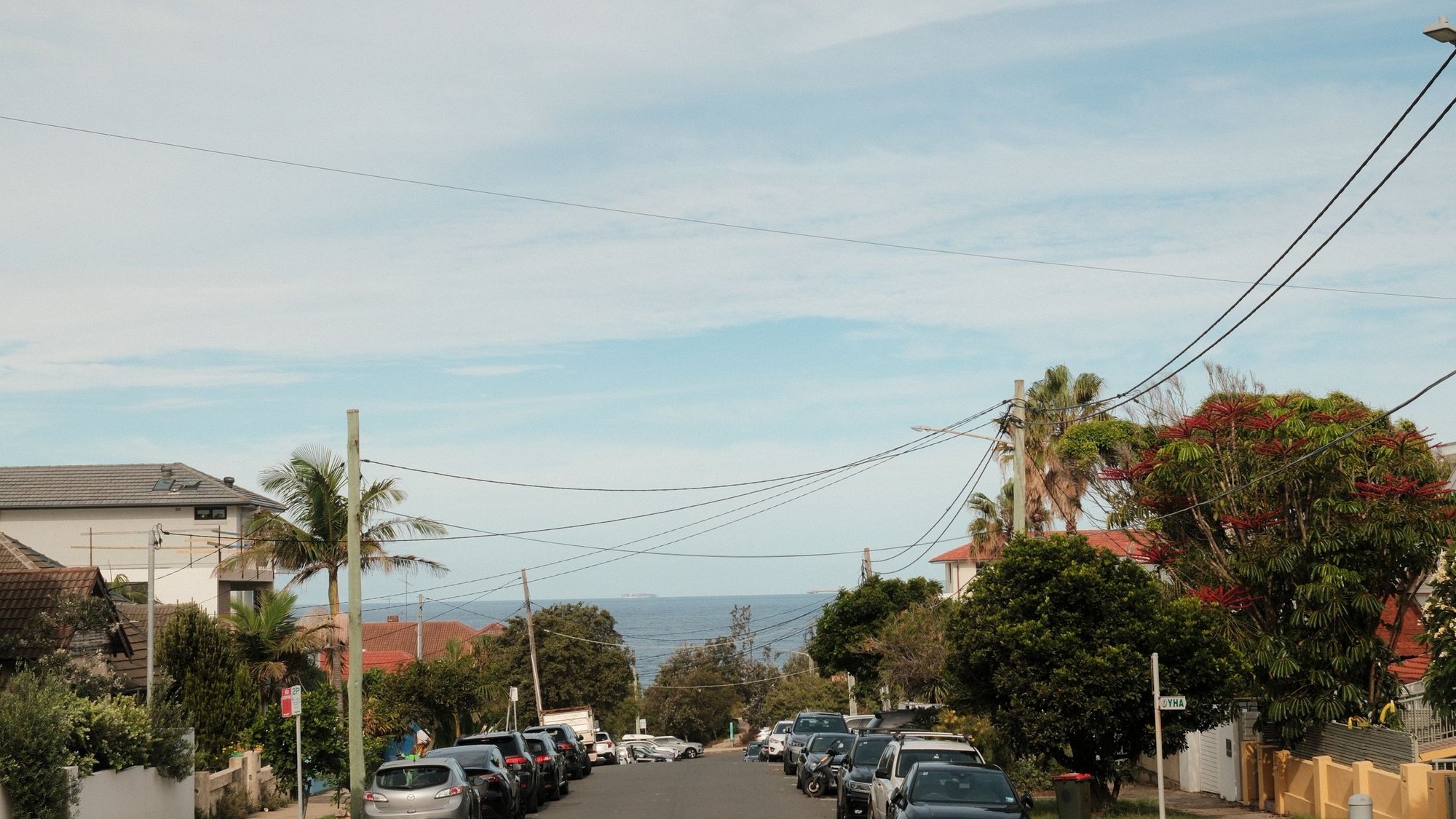A quiet Australian coastal street with parked cars and the ocean at the end of the road.