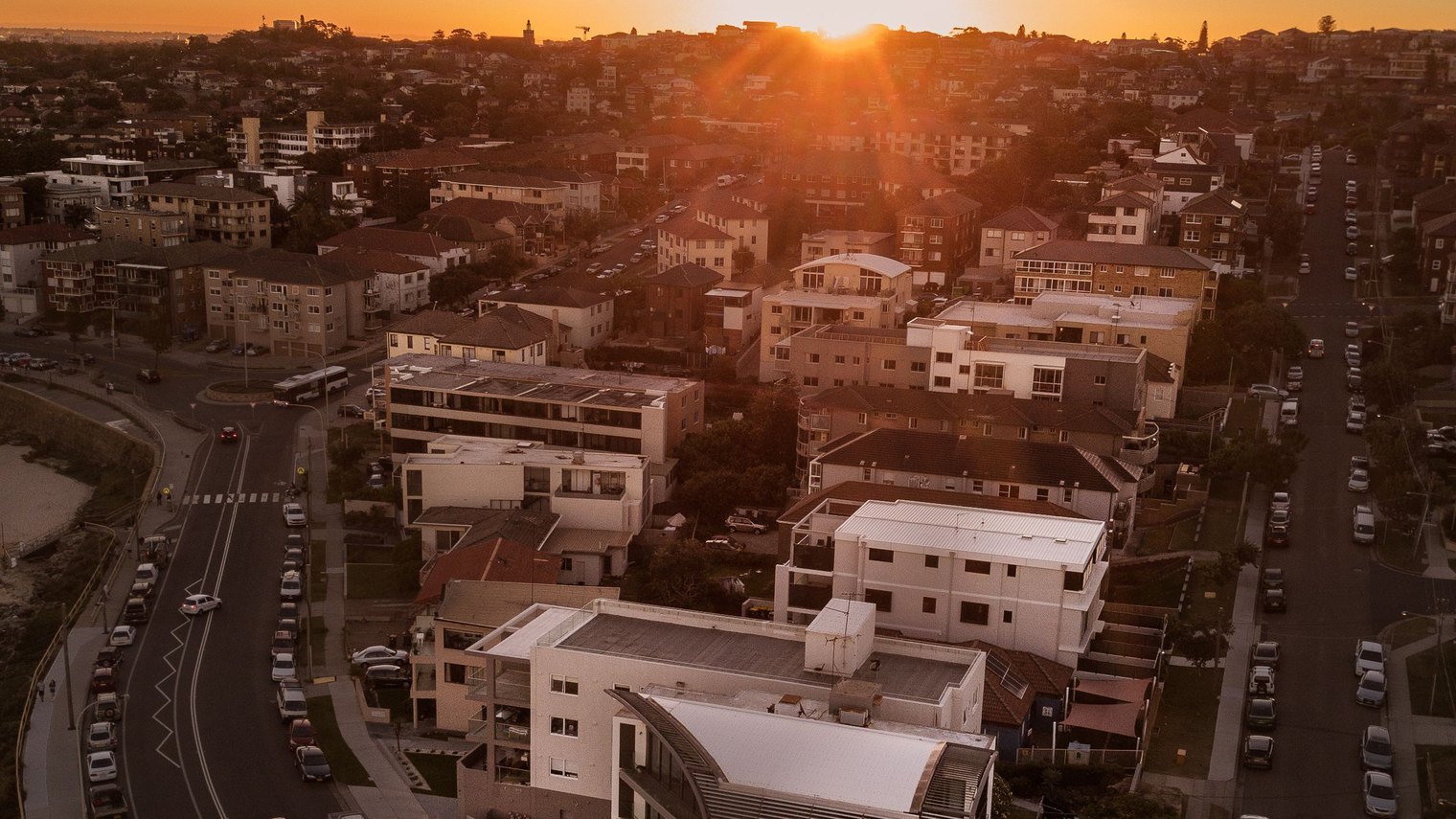 Aerial view of an Australian coastal suburb at sunset with the beach and headland beyond.