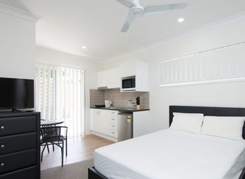 Inside a modern Australian rooming house room with a bed, desk and small kitchenette